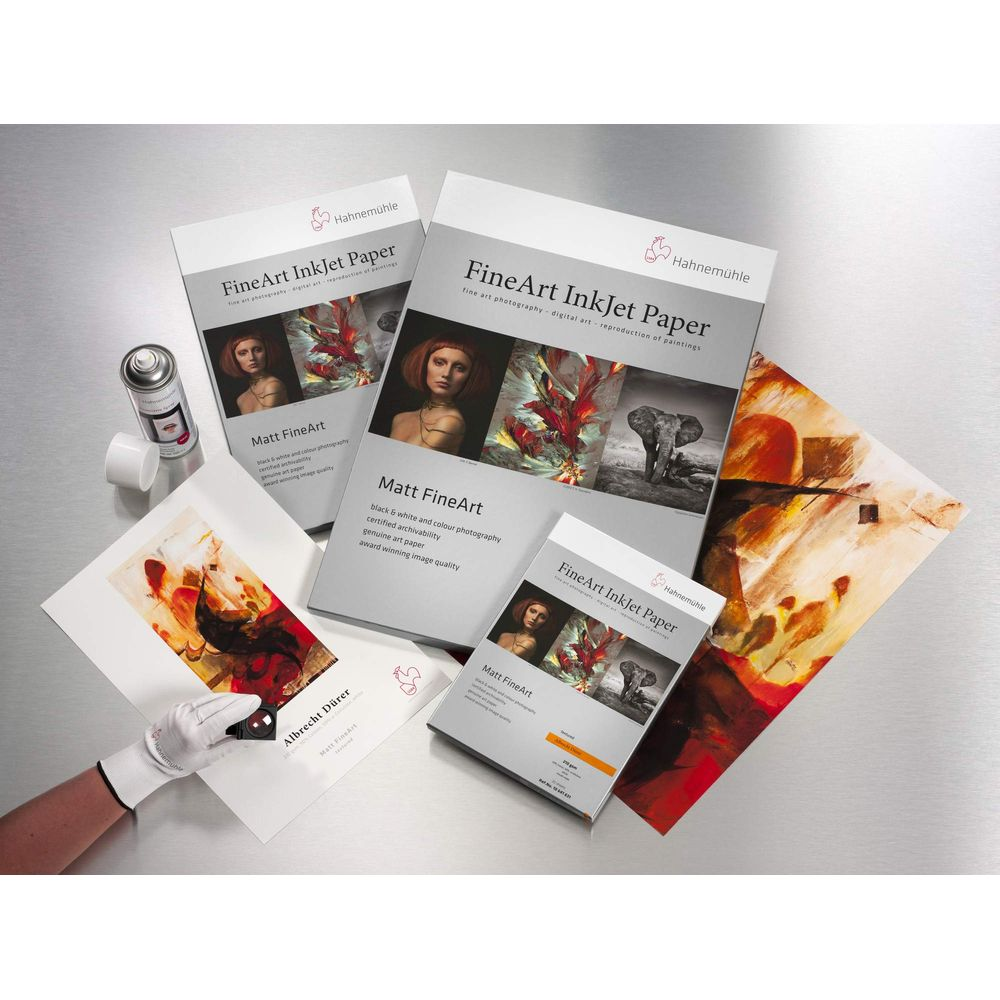 Hahnemühle FineArt InkJet Paper Packungen und Drucke auf einem Tisch. Eine Hand in einem weißen Handschuh hält einen Druck.
