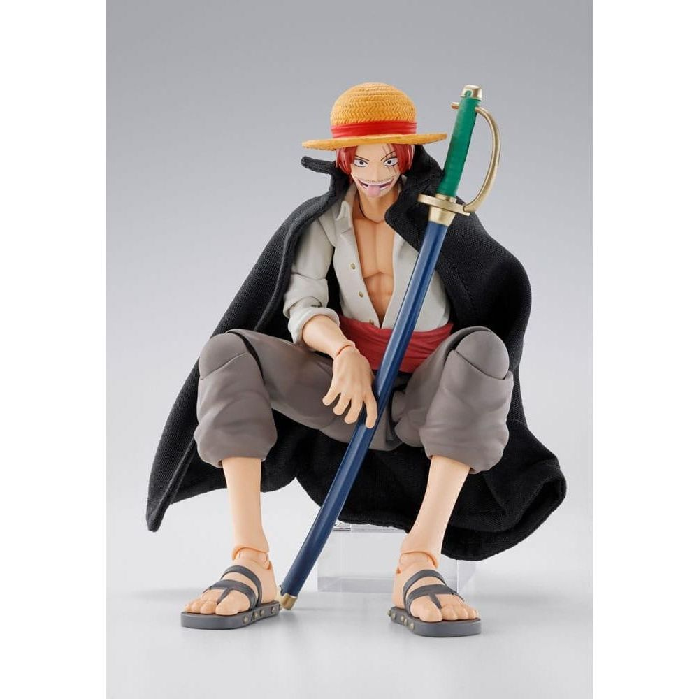 Una figura de acción sentada con sombrero de paja, capa negra, cinturón rojo y espada.