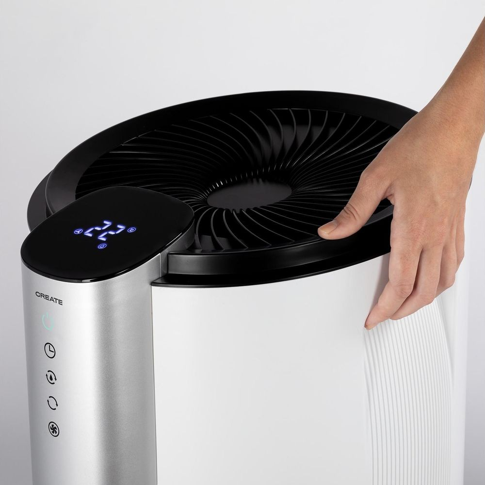Una mano toca un purificador de aire blanco con ventilador negro y pantalla digital.