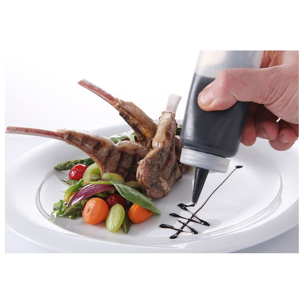 Uno chef guarnisce costolette d'agnello e verdure con glassa balsamica da una bottiglia.