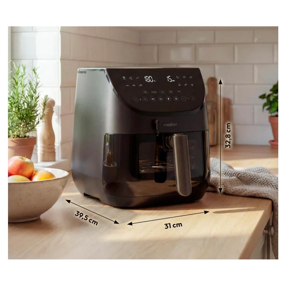 Zwarte airfryer met digitale displays, naast een fruitschaal en planten.