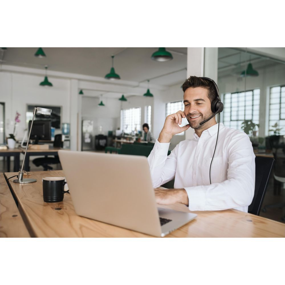 Homme en chemise blanche avec casque parle sur ordinateur portable dans un bureau.