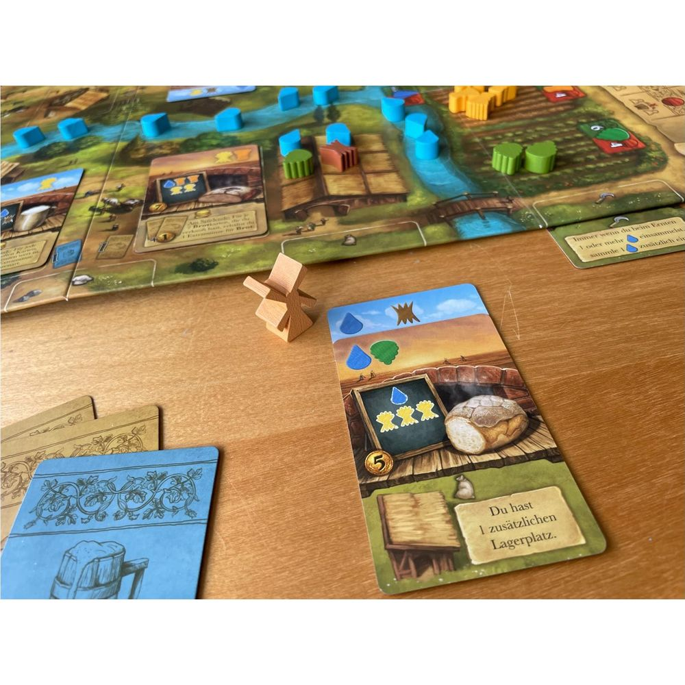 Ein Brettspiel mit Spielsteinen und Karten. Ein kleiner Holzwindmühlen-Spielstein liegt vorne.