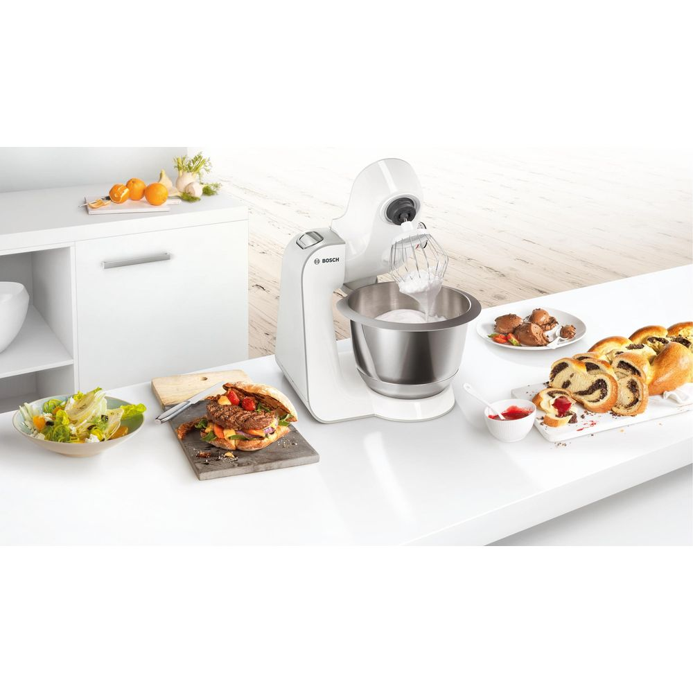 Ein weißer Küchenmixer mit Schüssel, daneben ein Burger, Salat und Gebäck.