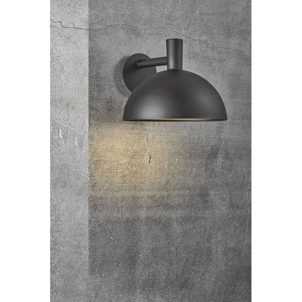 Eine dunkelgraue, kuppelförmige Außenwandleuchte ist an einer strukturierten Betonwand montiert.