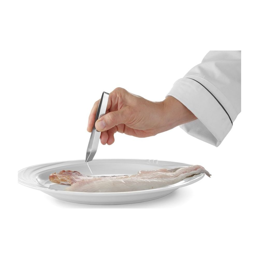 Uno chef usa una pinza per rimuovere le lische da un filetto di pesce su un piatto.