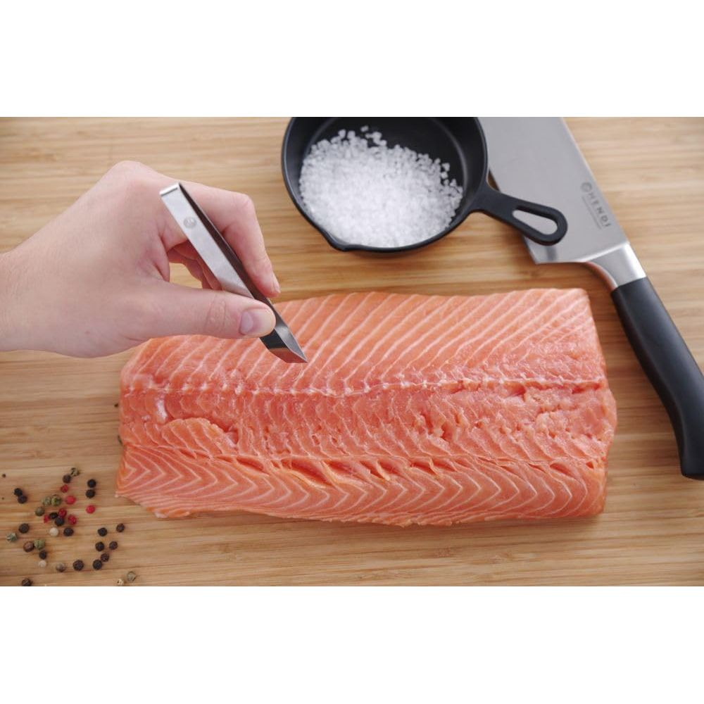 Un filetto di salmone su un tagliere, preparato con pinzette, sale e coltello.