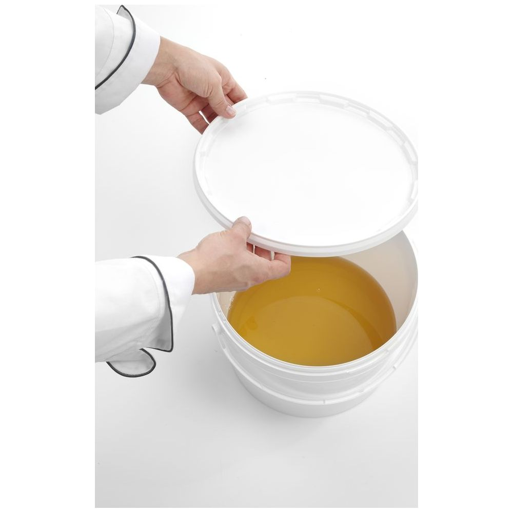 Una persona in abiti da chef solleva un coperchio bianco da un secchio di liquido giallo.