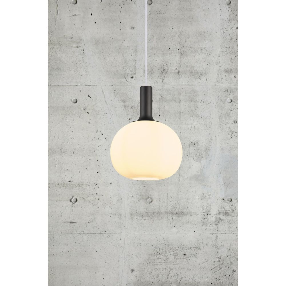 Une lampe ronde et laiteuse pend à une tige noire devant du béton.