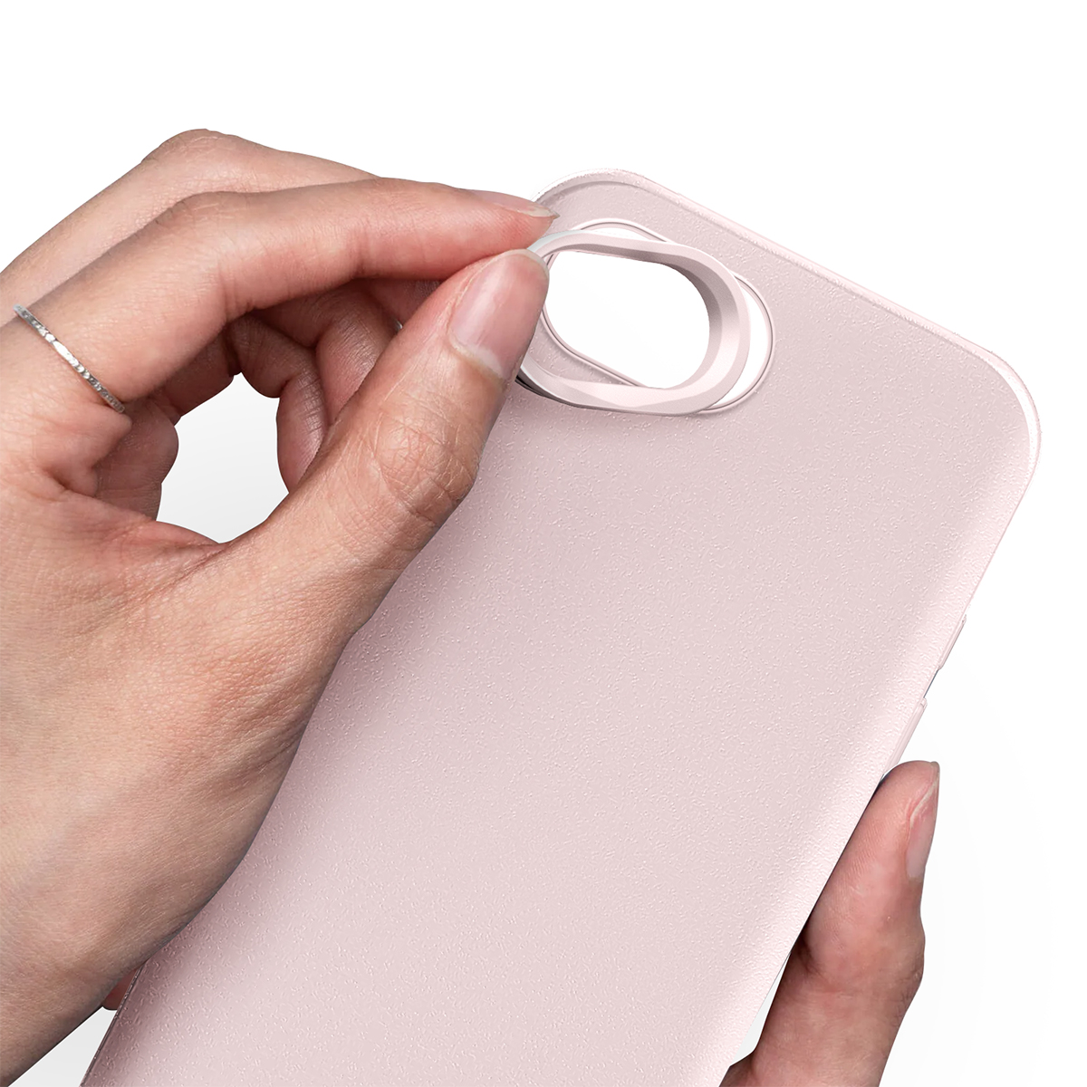 Une main avec une bague fixe un anneau de protection rose sur une coque de téléphone.
