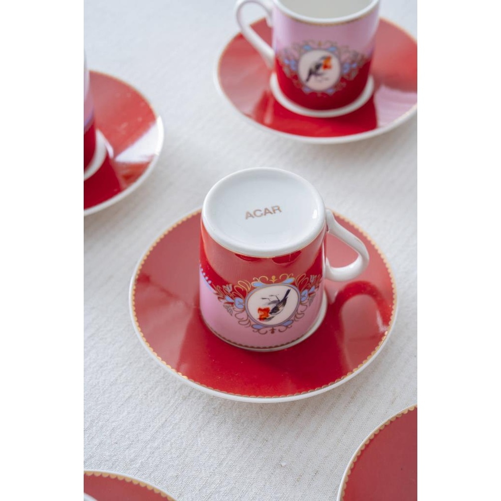 Kırmızı ve pembe kahve fincanları, kuş motifli tabaklarda.