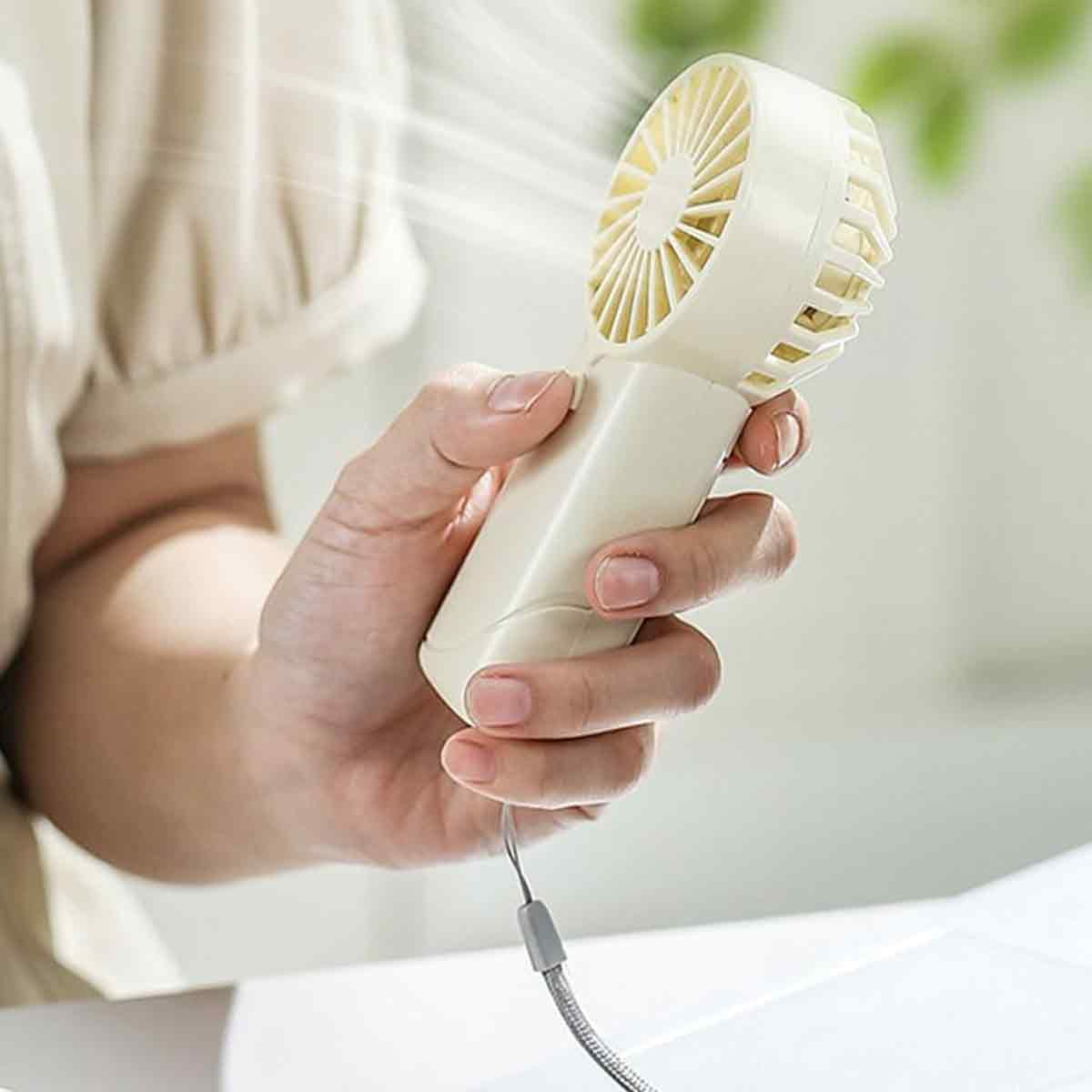 Eine Hand hält einen kleinen, cremefarbenen Ventilator, der Luft bläst.