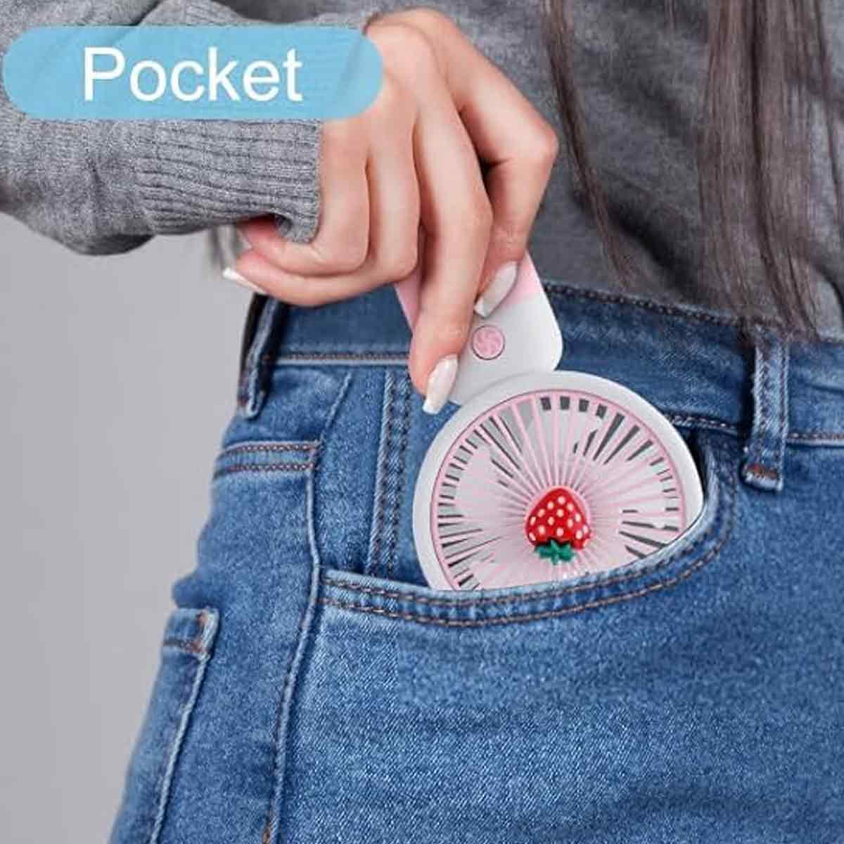 Eine Hand steckt einen kleinen, pinken Ventilator mit Erdbeermotiv in eine Jeanstasche.