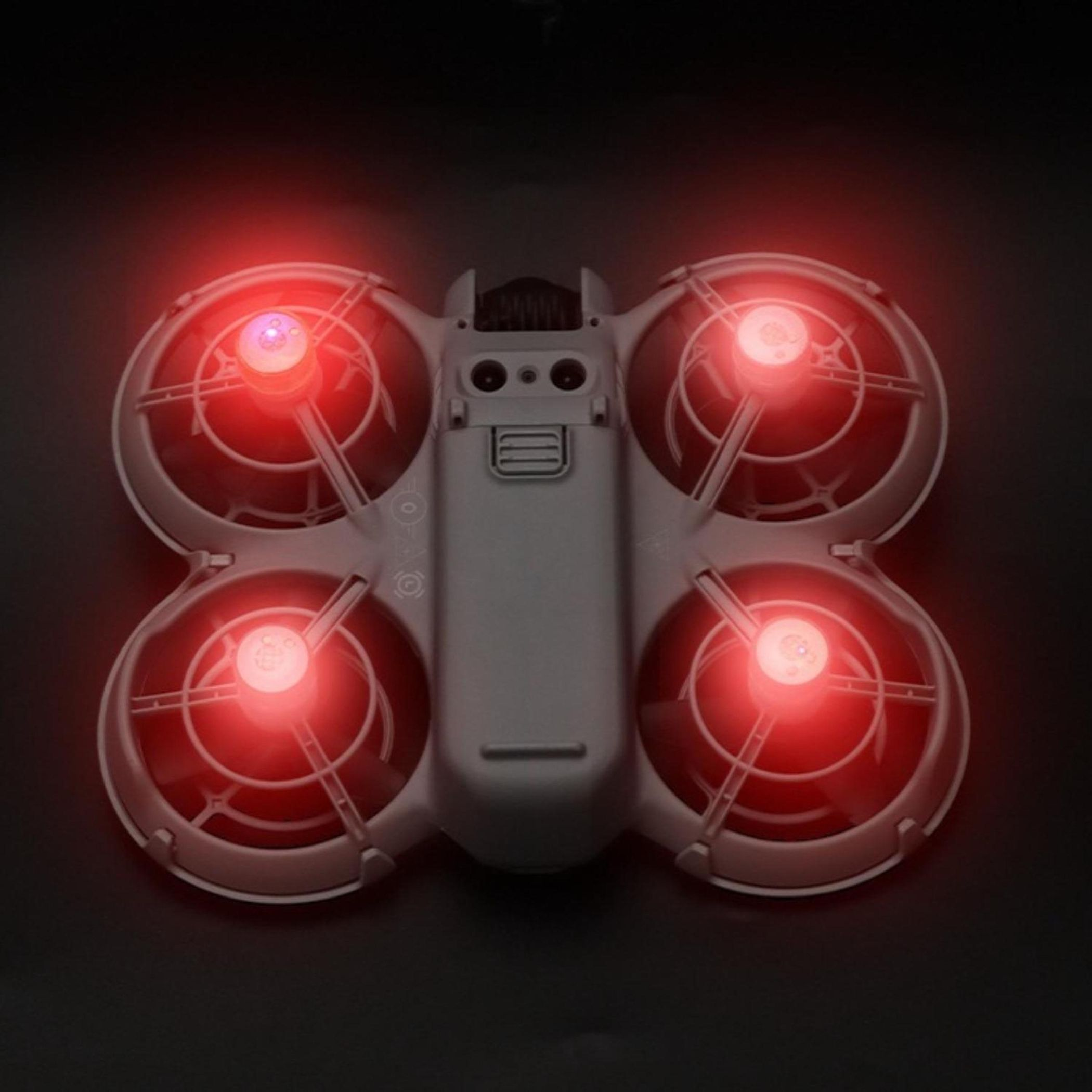 Ein weißer Quadrocopter mit roten Lichtern auf schwarzem Hintergrund.