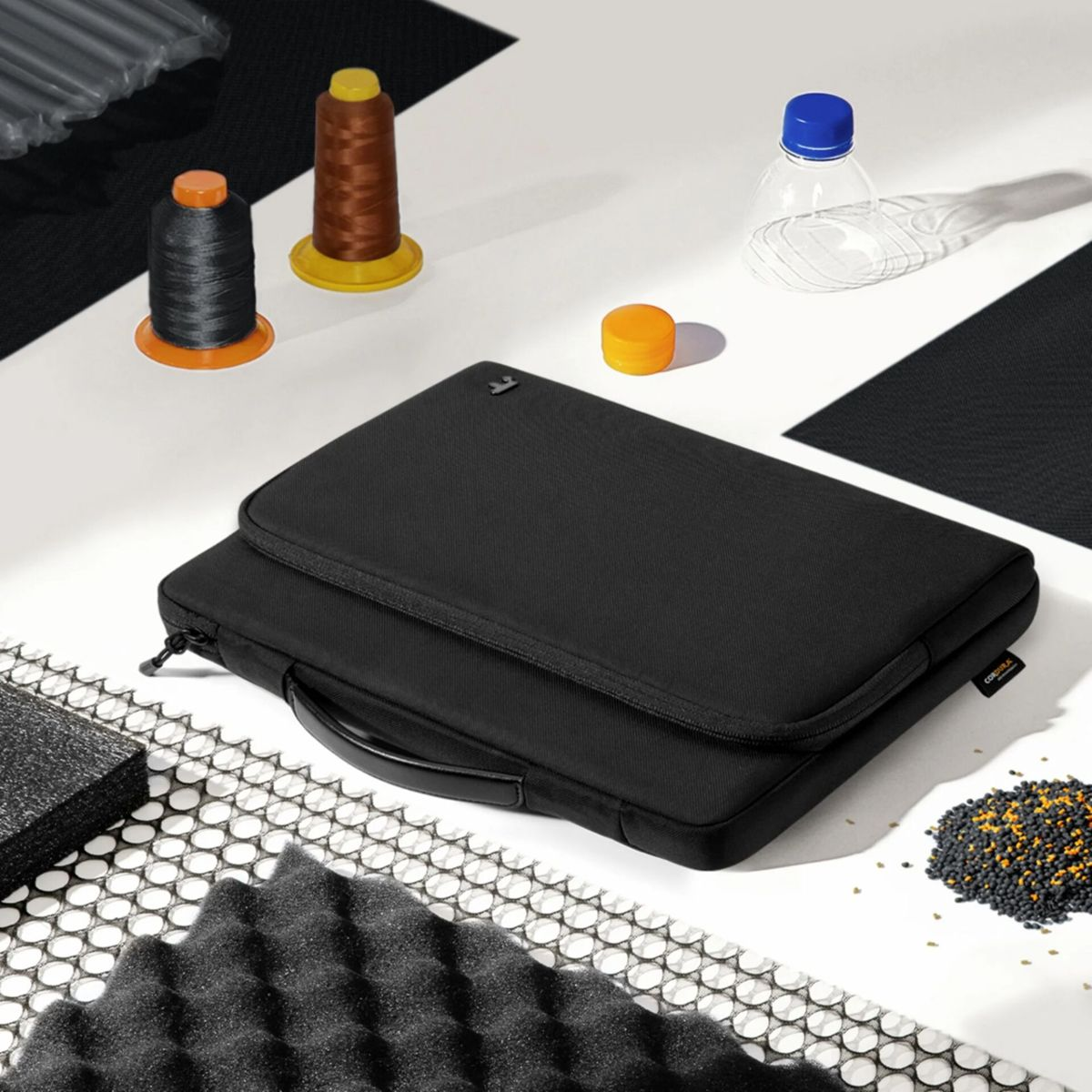 Borsa nera per laptop con rocchetti, tappo arancione, bottiglia e pellet.