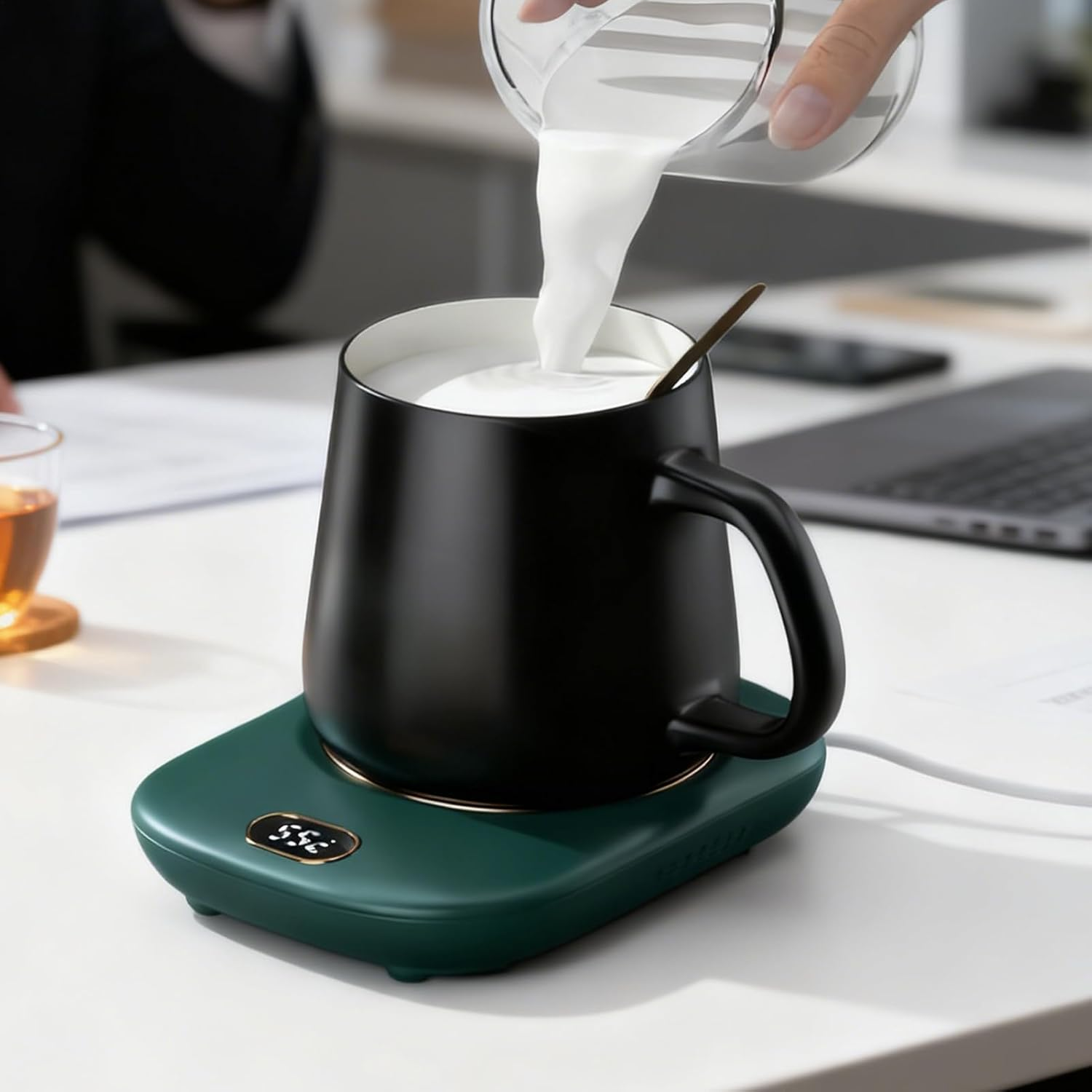 Milch wird in eine schwarze Tasse auf einem grünen Becherwärmer gegossen.