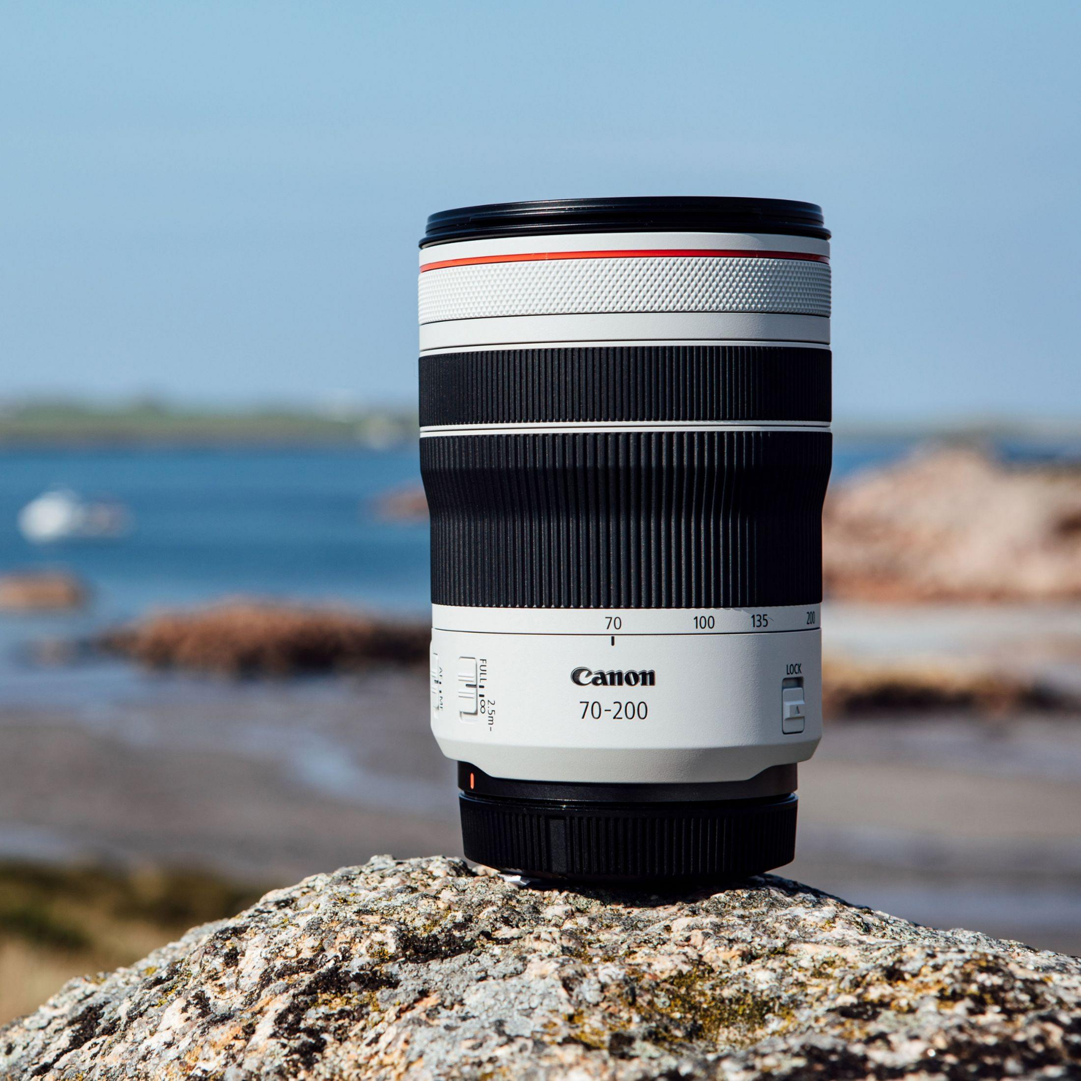 Un obiettivo Canon 70-200mm poggia su una roccia con uno sfondo sfocato di acqua e terra.