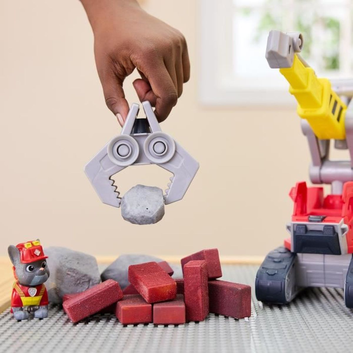 Un niño sostiene una roca con una garra. Un vehículo de construcción de juguete está cerca.