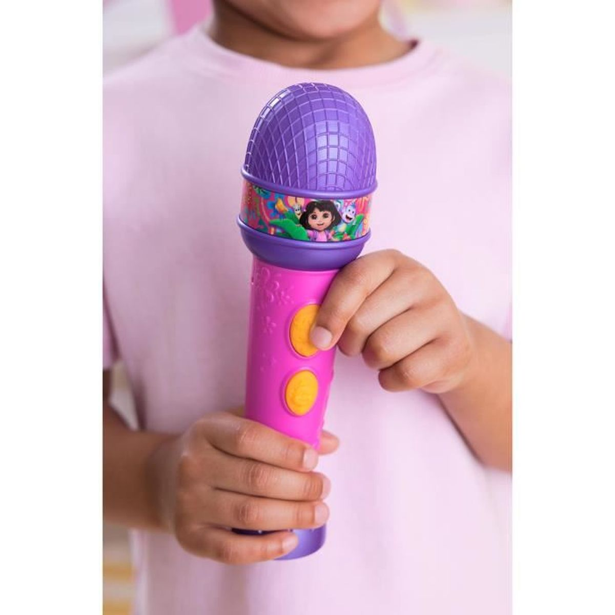 Ein Kind hält ein pinkes Mikrofon mit Dora-Motiv und lila Kappe. Zwei gelbe Knöpfe sind sichtbar.