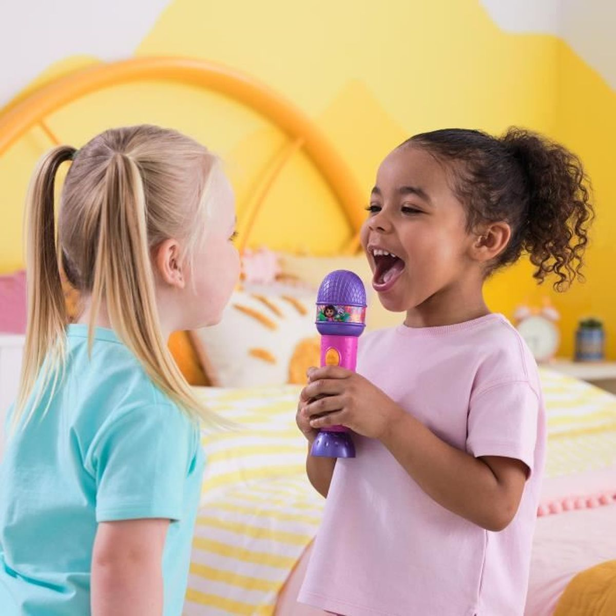 Zwei Mädchen singen in ein Mikrofon in einem gelben Zimmer.