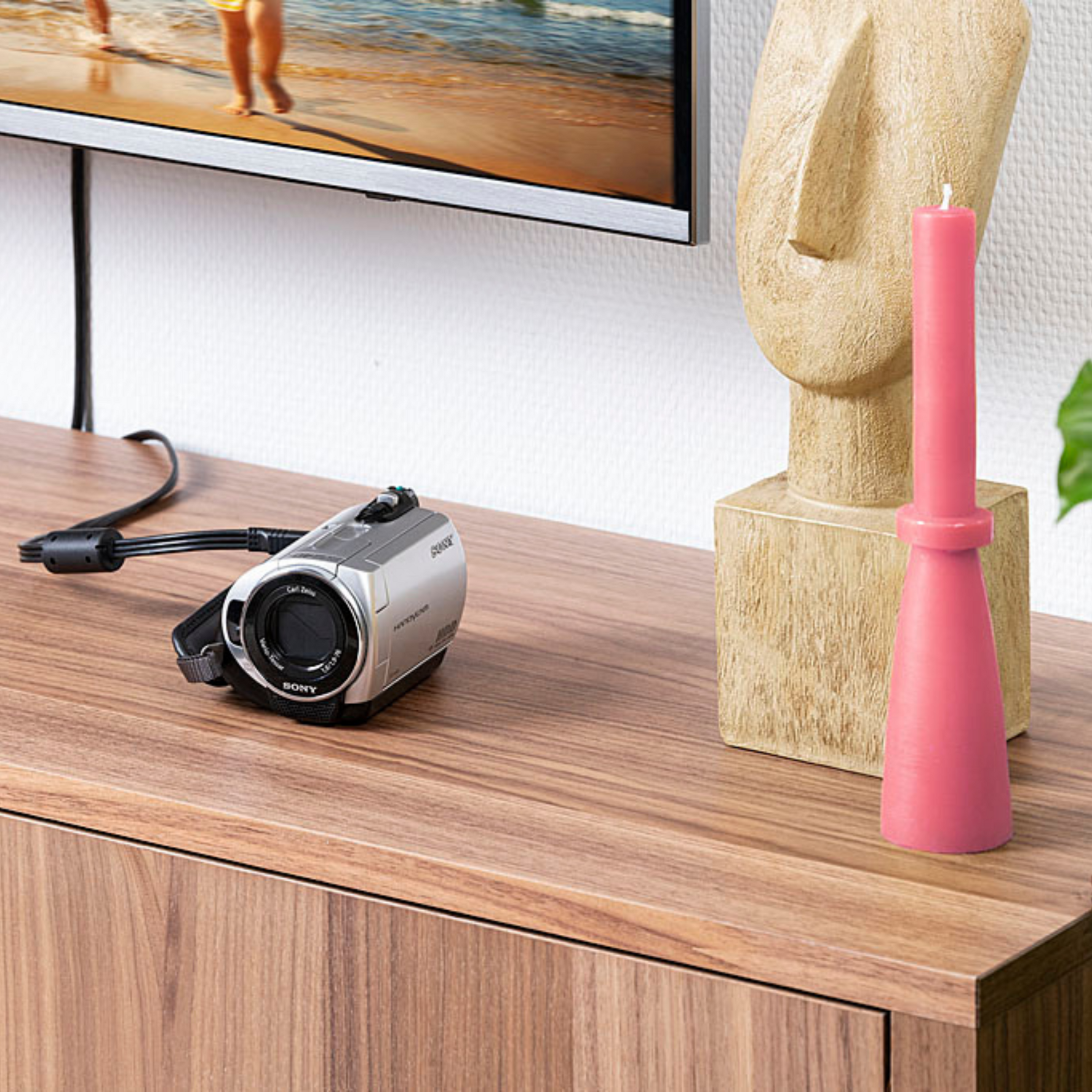 Ein silberner Camcorder und eine rosa Kerze auf einem Holzmöbel.