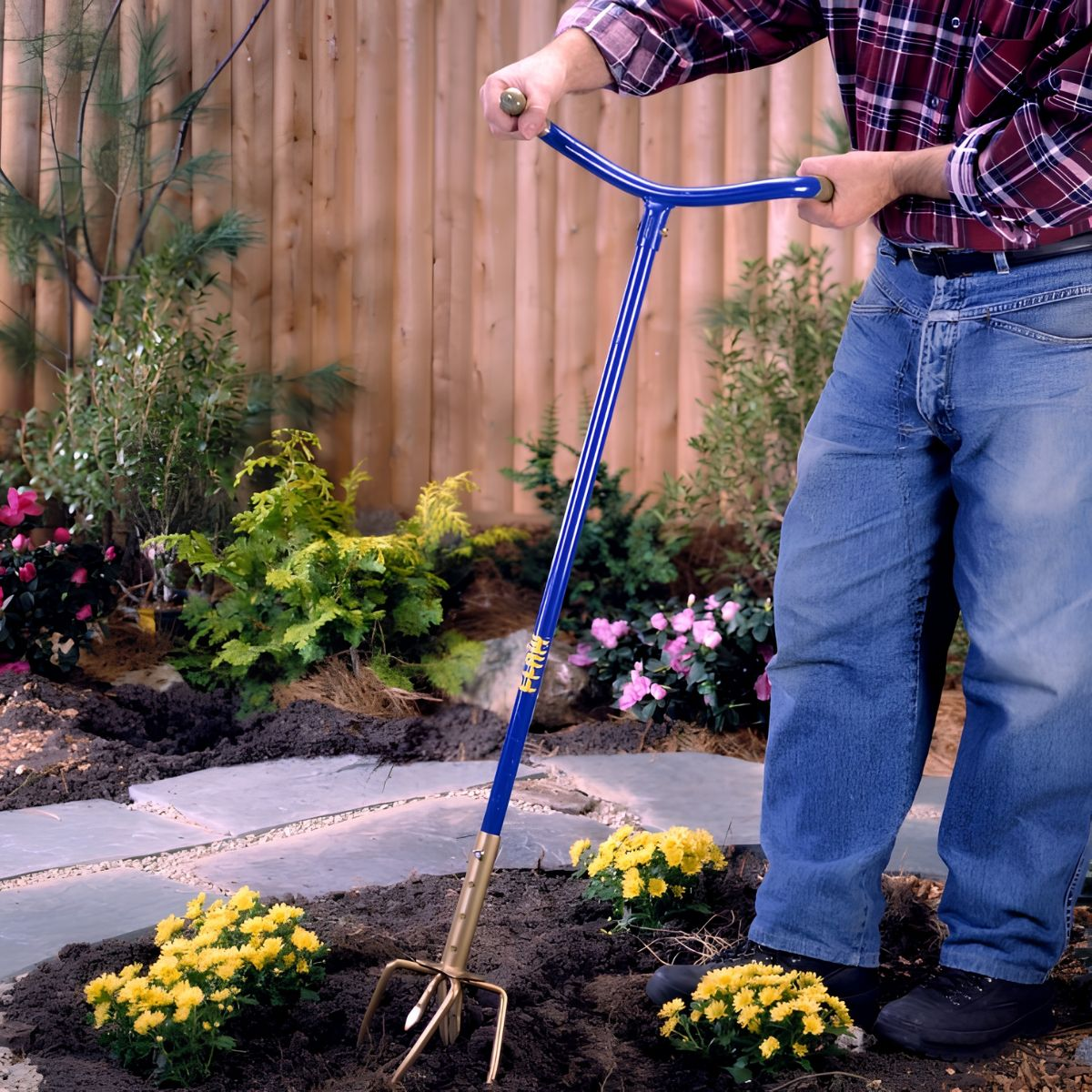 Man in spijkerbroek houdt blauw tuingereedschap vast in tuin.
