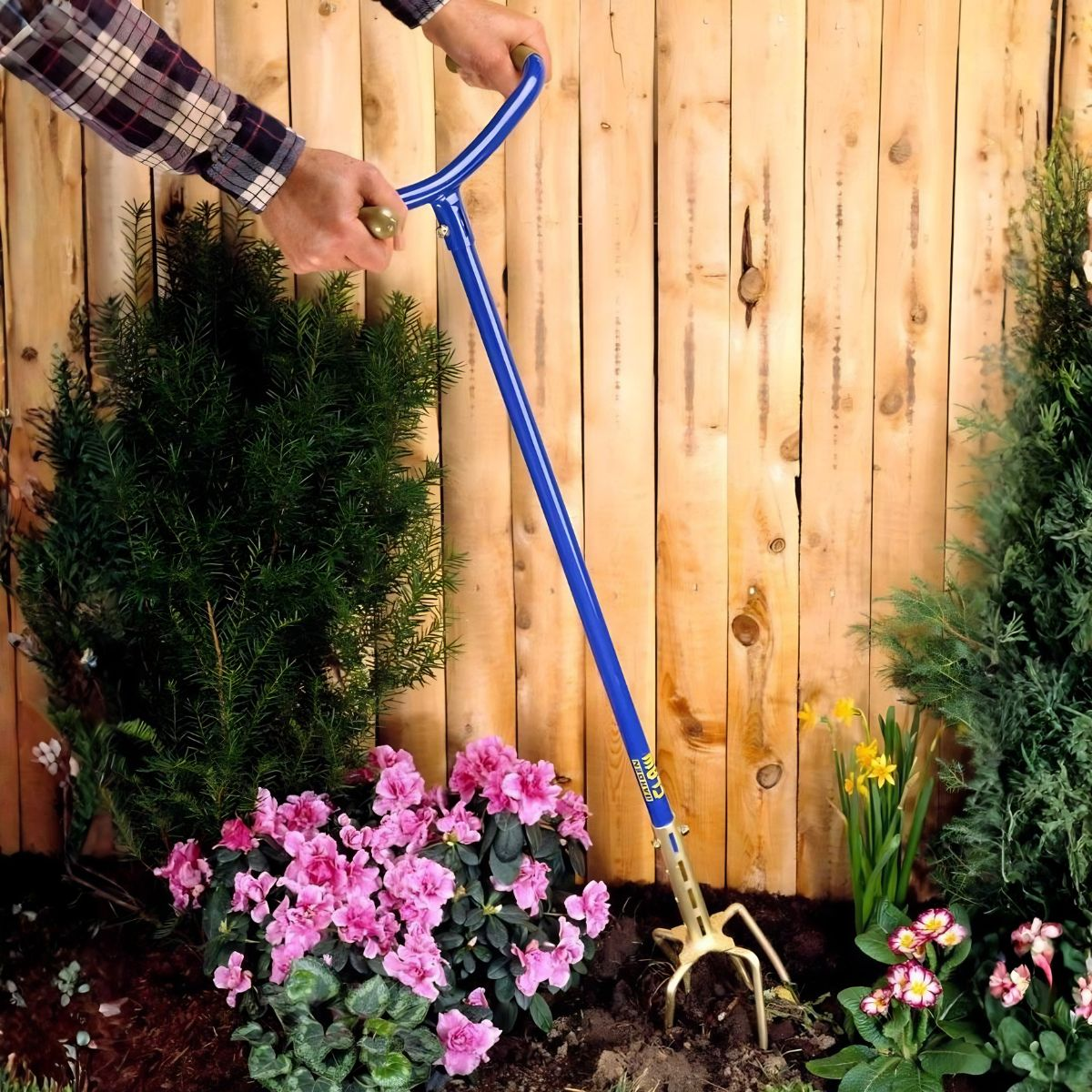 Tuinman gebruikt blauw gereedschap bij roze azalea's en houten hek.