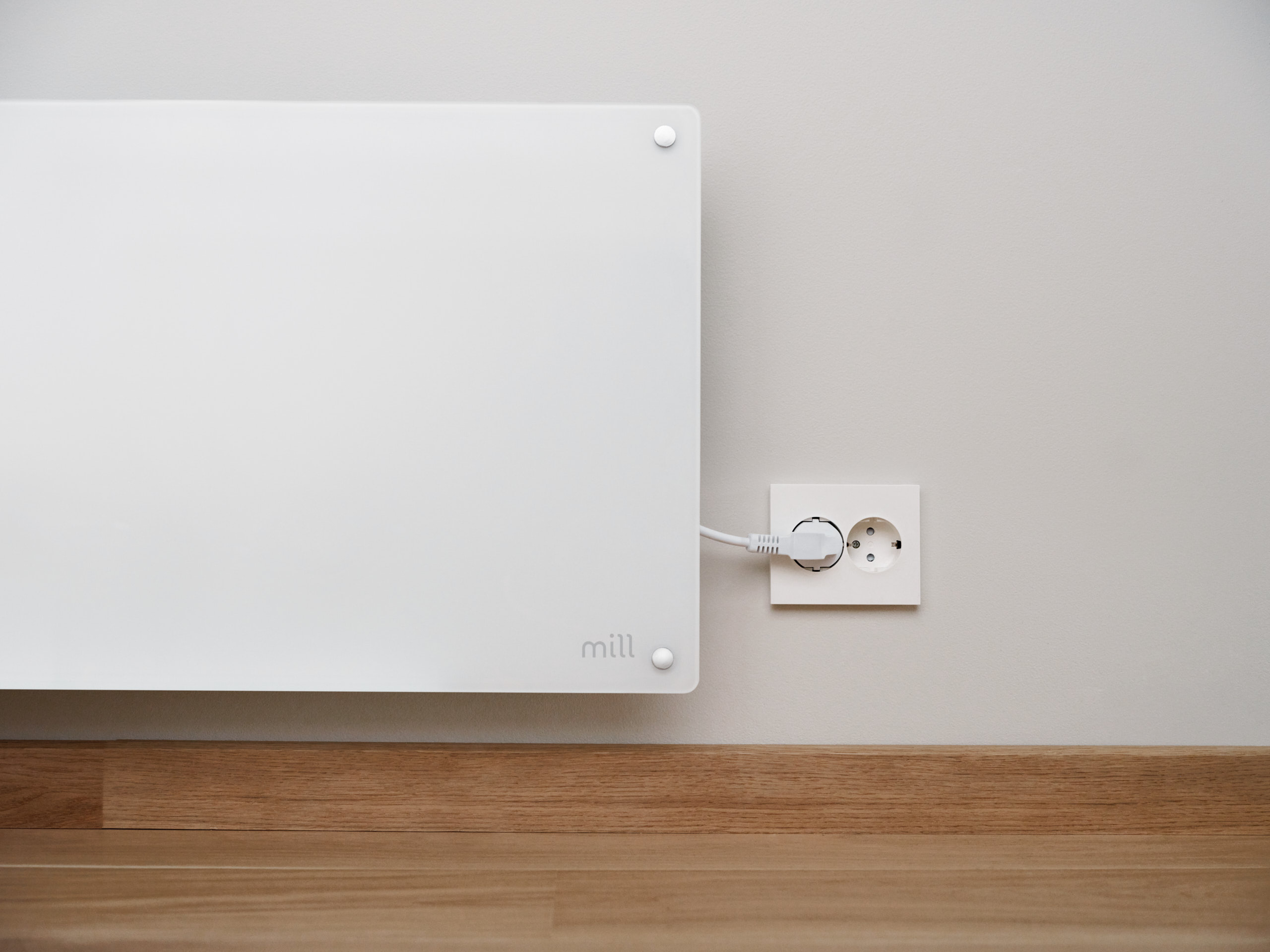 A white heater plugged into an outlet on a light gray wall.