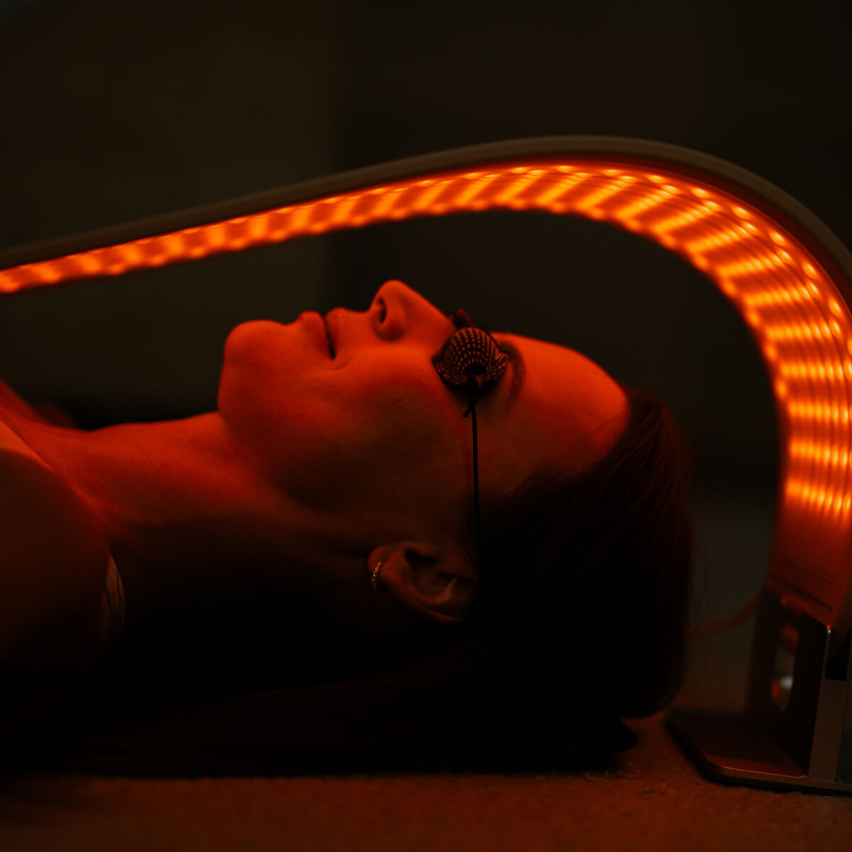 Una persona con gafas protectoras yace bajo un panel curvo de terapia de luz LED naranja.