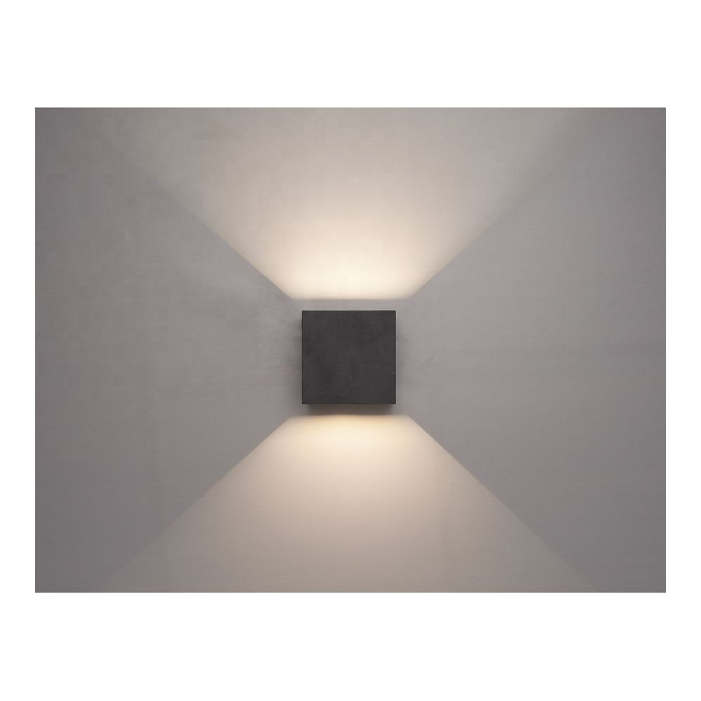 Un luminaire mural sombre en forme de cube projette de la lumière vers le haut et le bas.