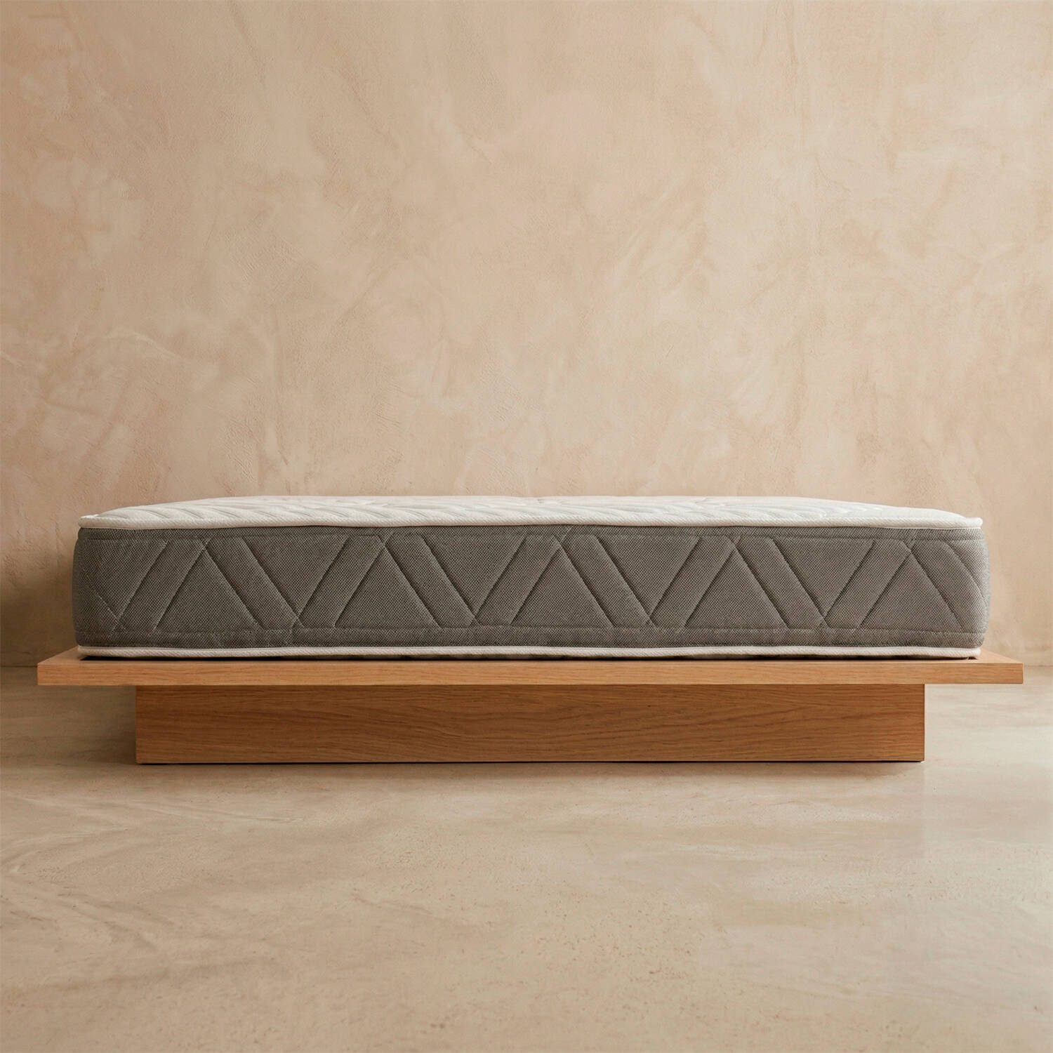Un colchón gris con patrones geométricos descansa sobre un marco de cama de madera.
