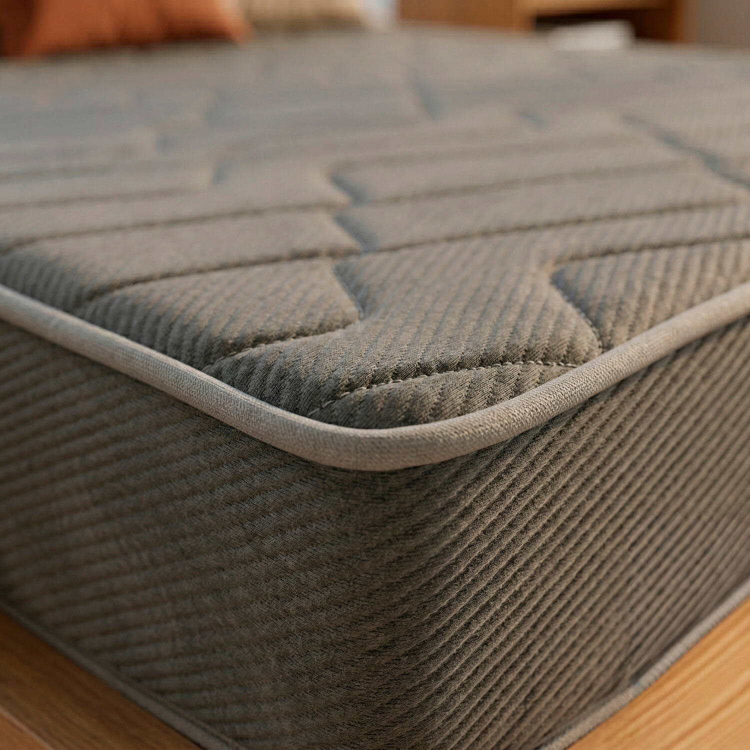 Borde de colchón gris con acolchado sobre suelo de madera.