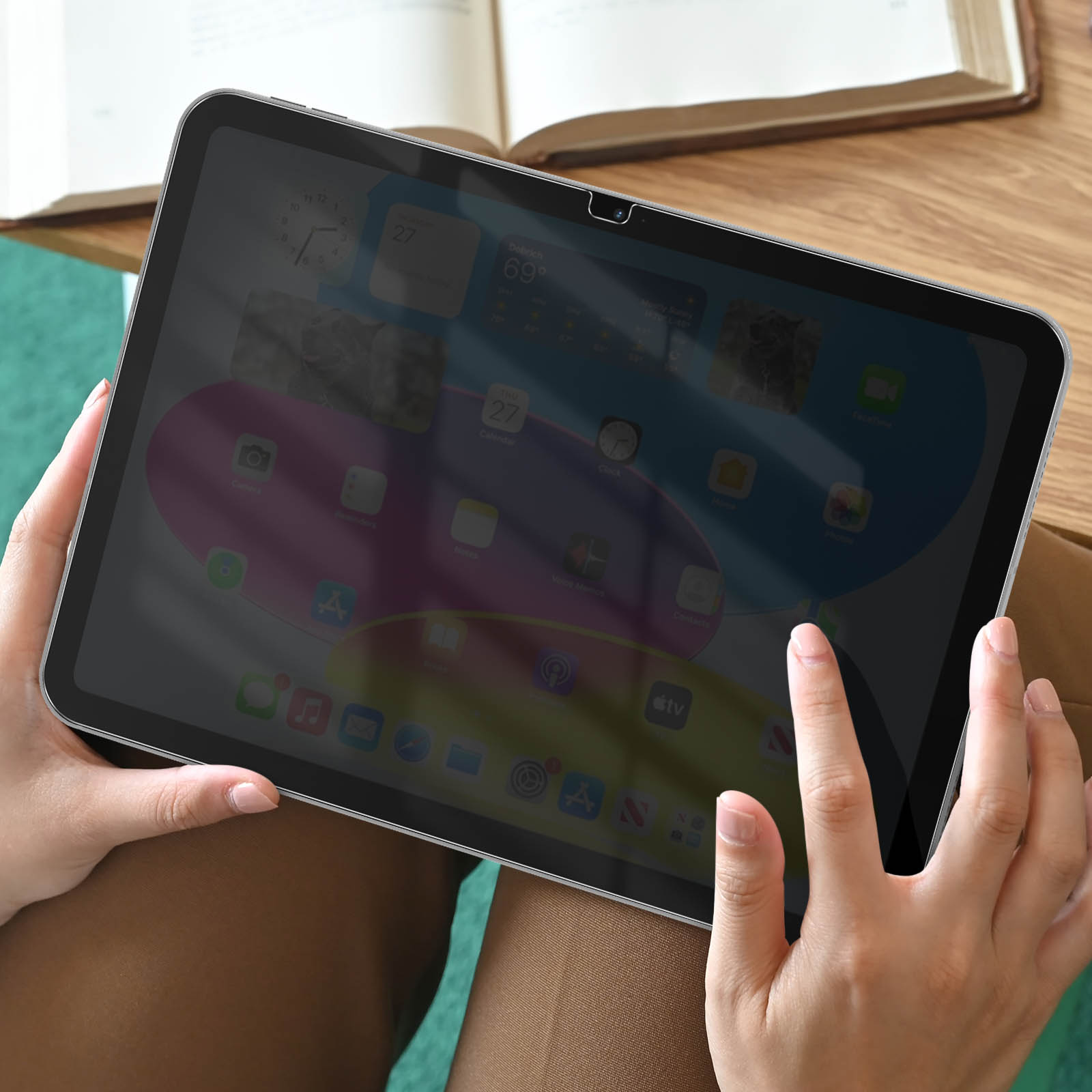 Mains tenant une tablette affichant des applications et des widgets. Un livre en arrière-plan.