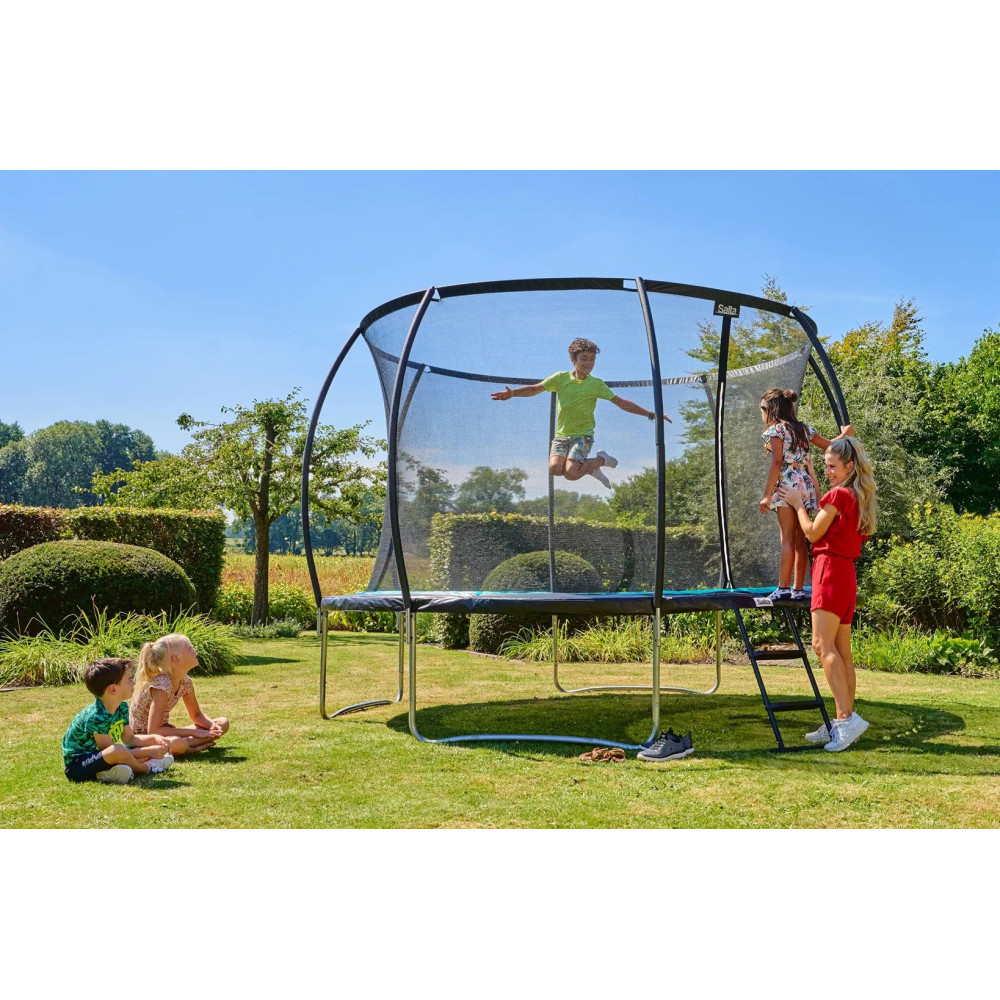 Dzieci skaczą na trampolinie w ogrodzie, podczas gdy inne patrzą.