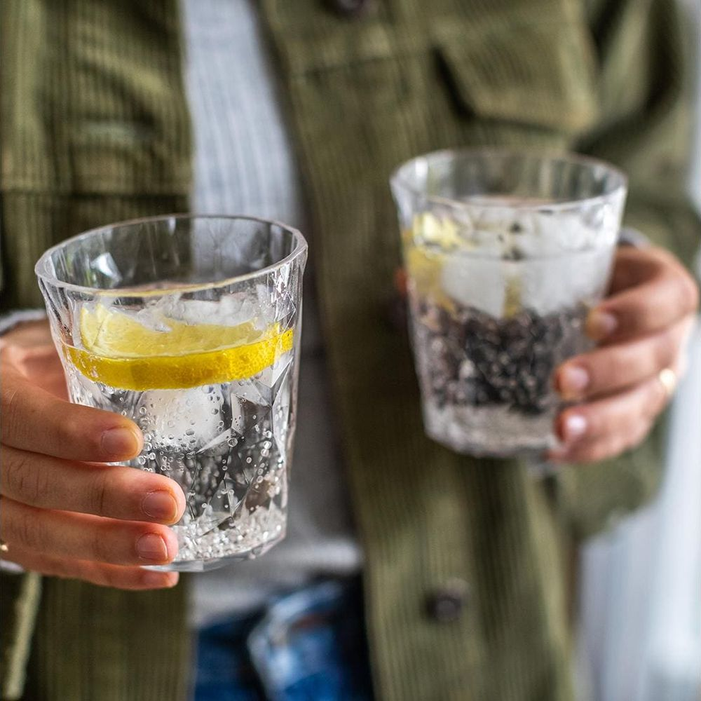 Zwei Gläser mit Wasser, Eis und Zitrone werden von Händen gehalten.