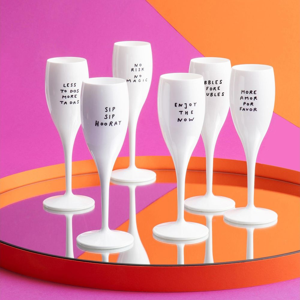 Sechs weiße Champagnerflöten mit Text auf einem Spiegeltablett. Rosa und orangefarbener Hintergrund.