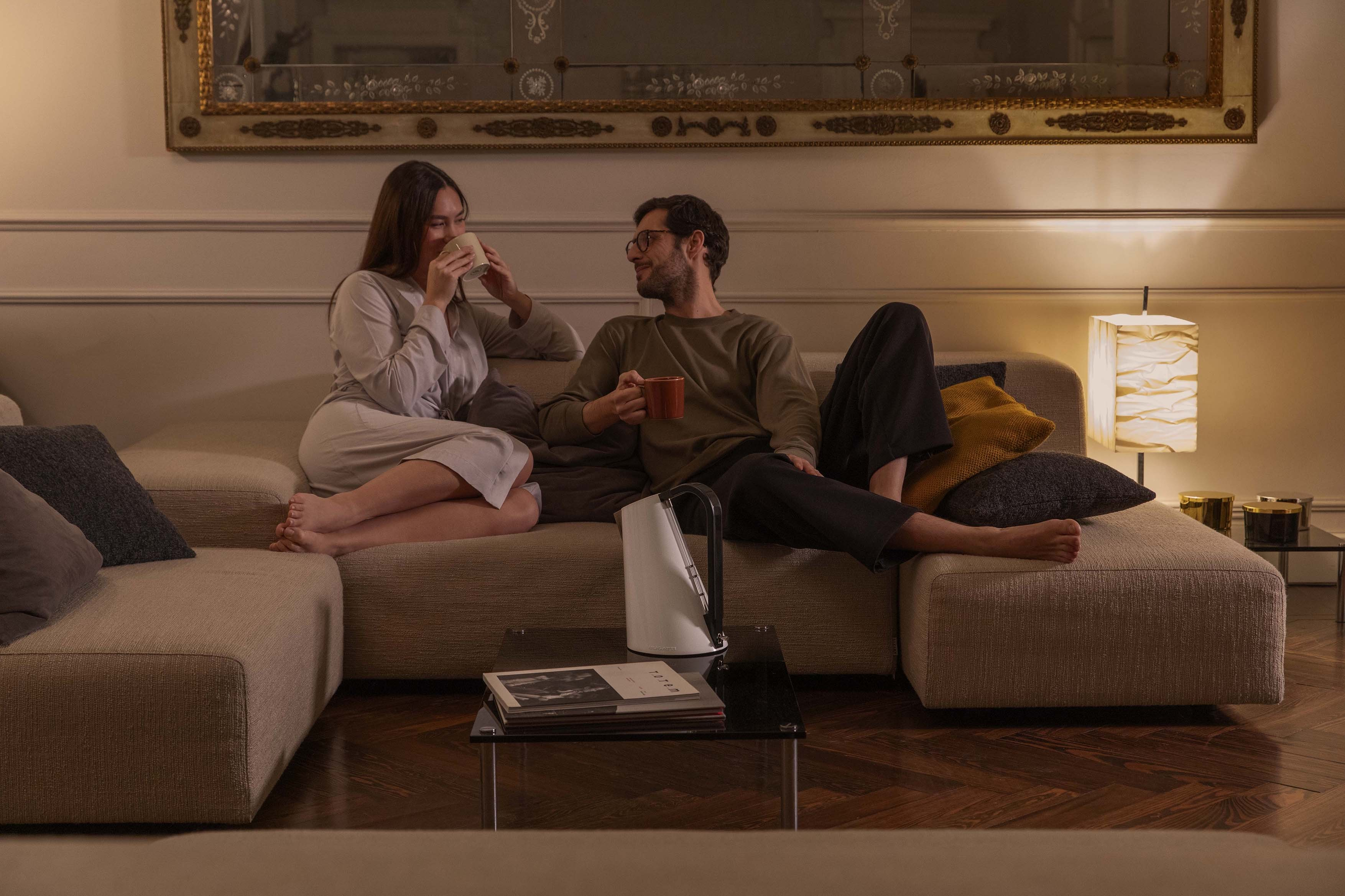 Un uomo e una donna siedono su un divano, bevendo da tazze.