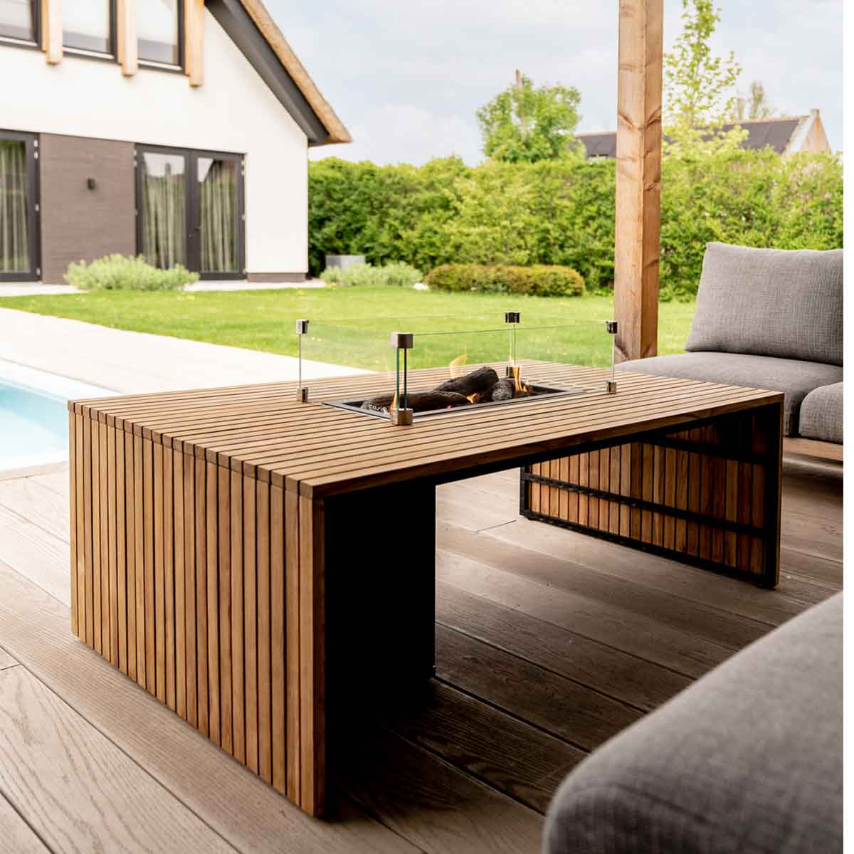 Wooden table with built-in fire, glass surround, on a deck with sofa.