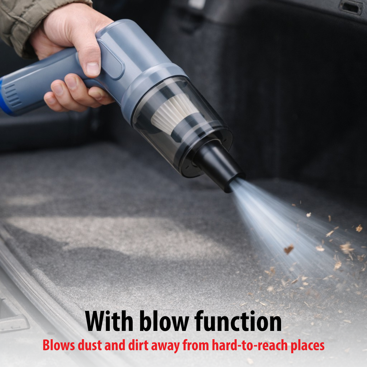 Hand holds gray handheld vacuum blowing dust out of a car trunk.