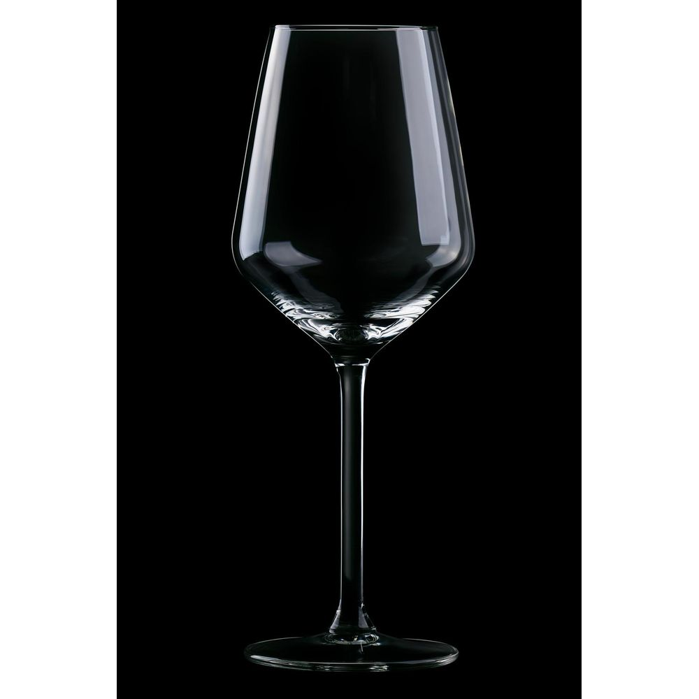 An empty, clear wine glass with a long stem stands against a black background.