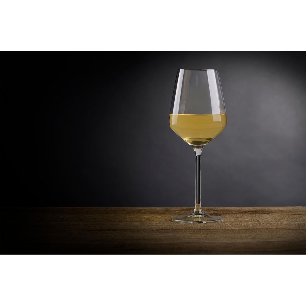 A glass of white wine sits on a wooden table against a dark background.