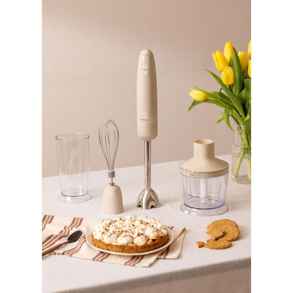 Una batidora de inmersión beige con batidor, vaso, picadora, pastel y tulipanes.