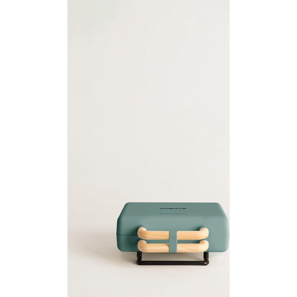 Una sandwichera verde azulado con asas de madera descansa sobre un soporte negro.