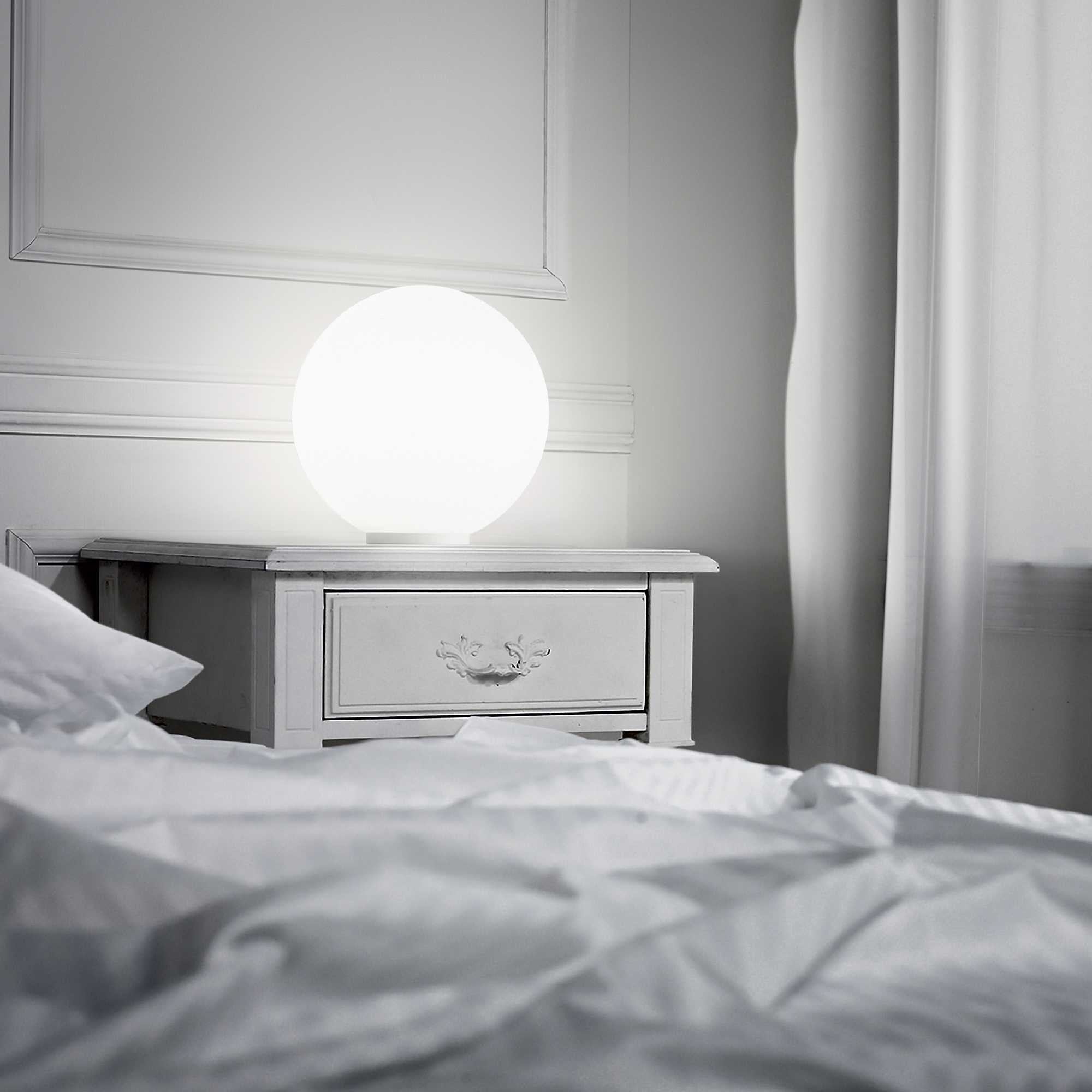 Comodino rotondo con cassetto e lampada. Biancheria da letto bianca in primo piano.
