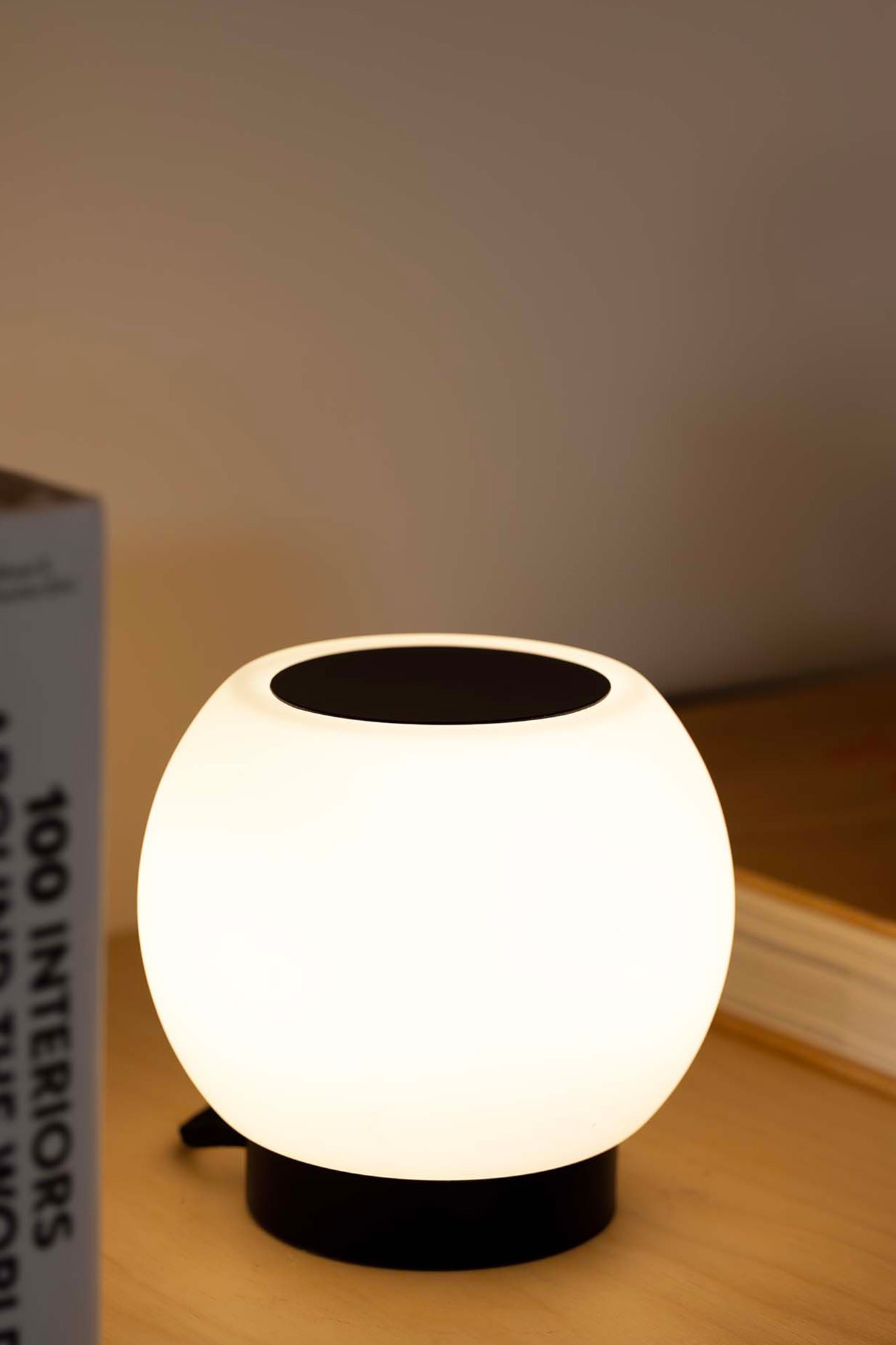 Una lampada sferica bianca luminosa con base nera su un tavolo di legno.
