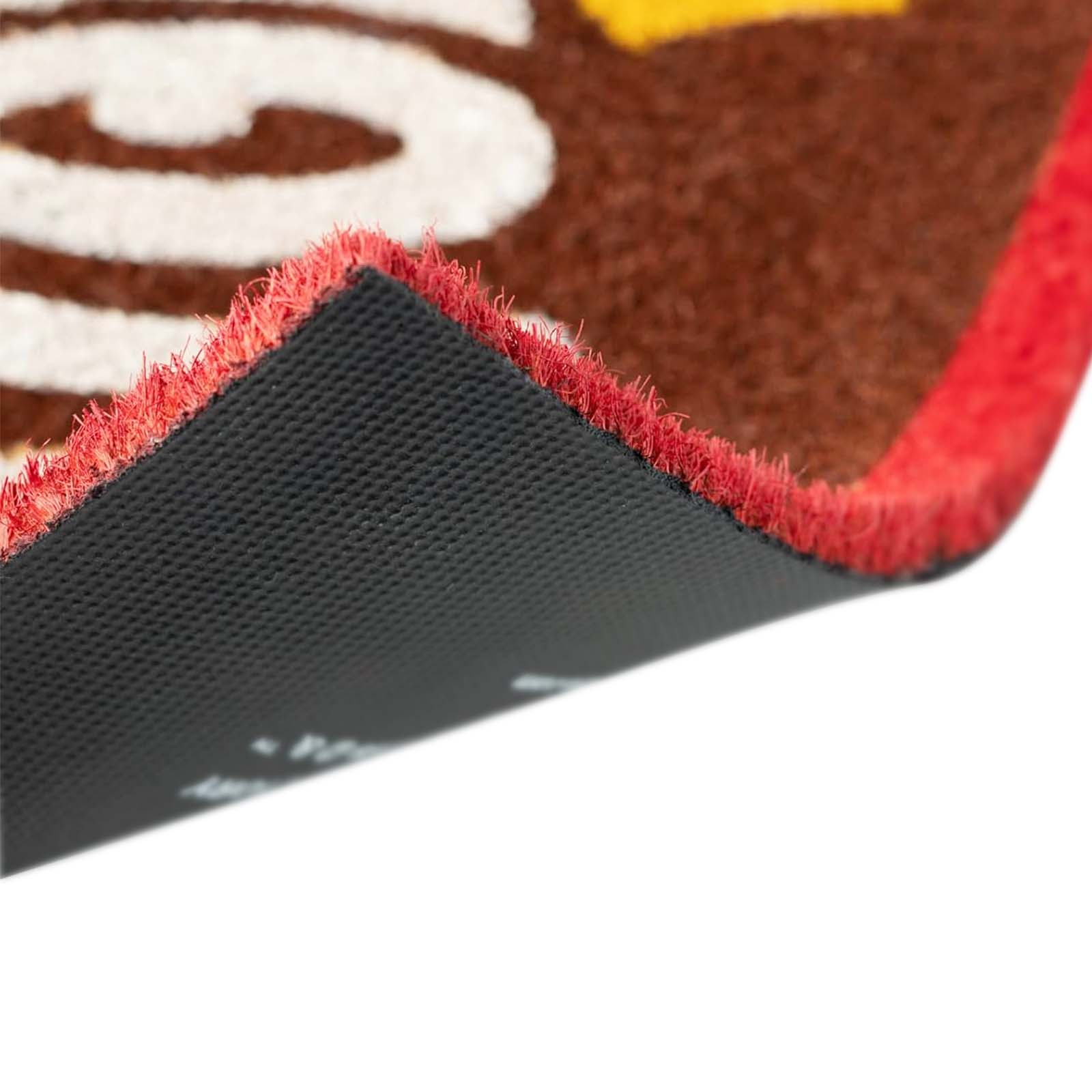 Angolo di uno zerbino in primo piano. Fibre marroni, vortici bianchi, bordo rosso, retro nero.