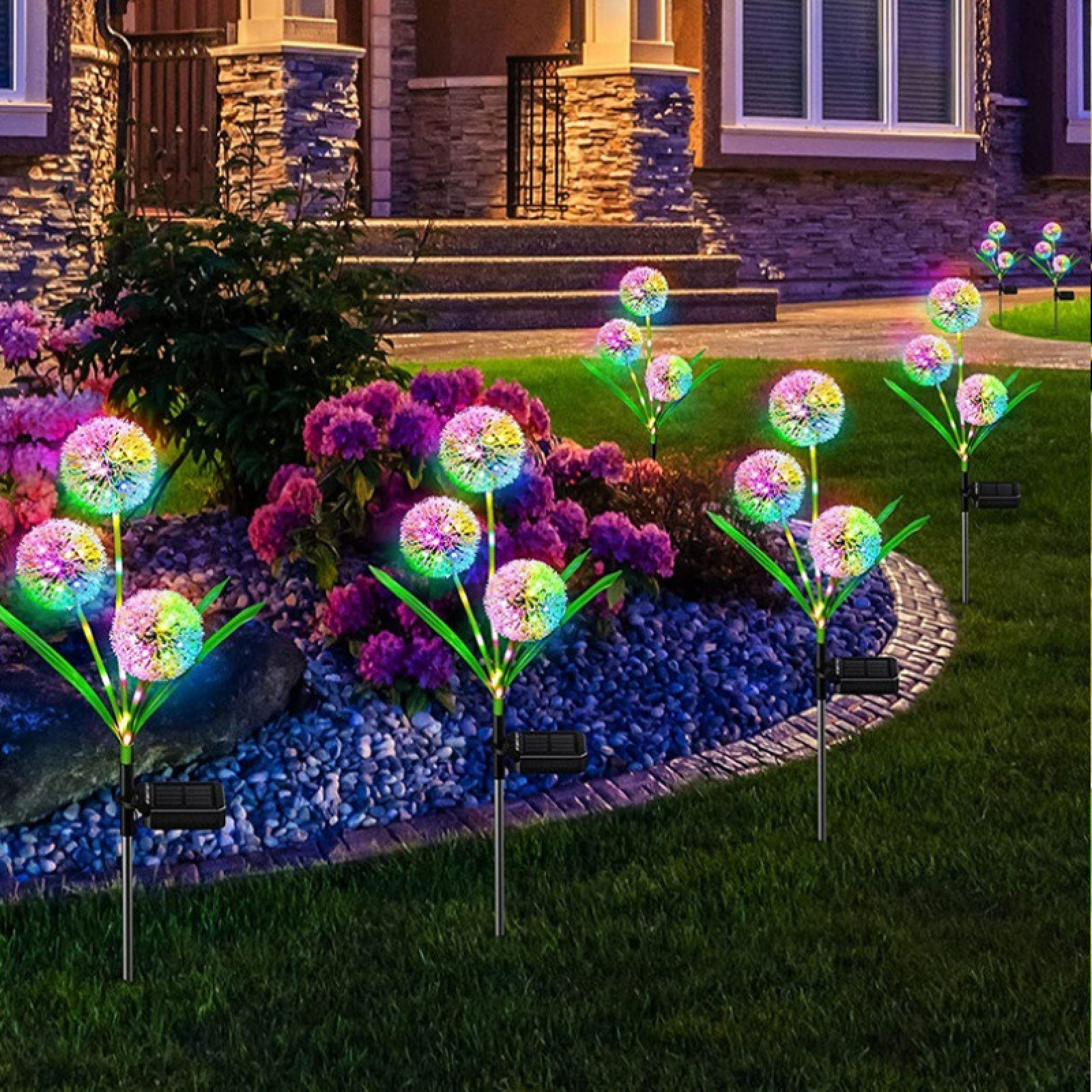 Bunte Solarleuchten in Löwenzahnform beleuchten einen Vorgarten mit Blumen und Steinen.