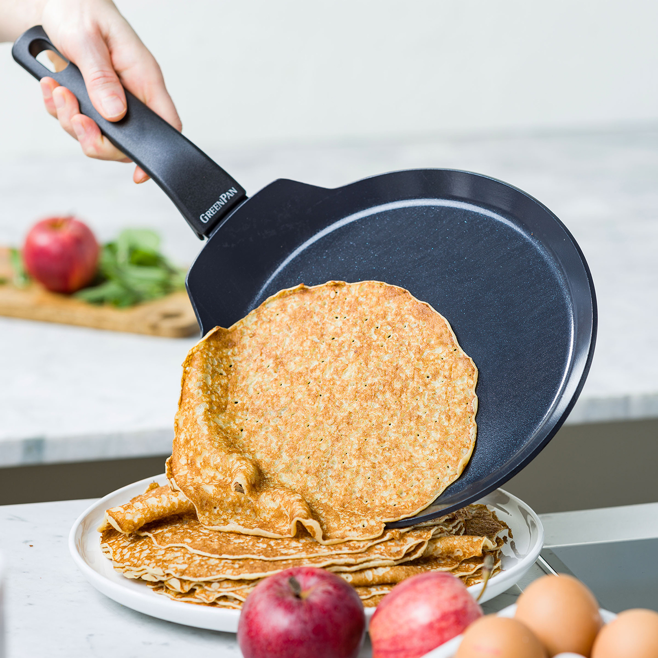Eine Person legt einen Pfannkuchen mit einer Pfanne auf einen Teller mit vielen Pfannkuchen.