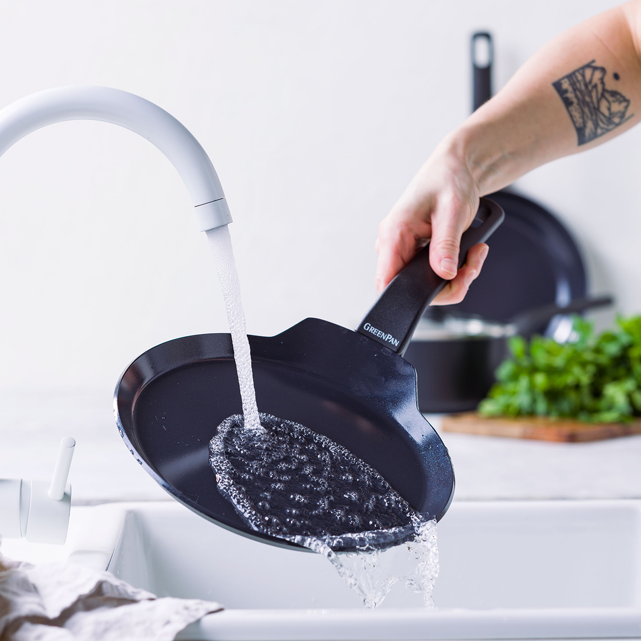 Eine Person reinigt eine schwarze Pfanne unter fließendem Wasser in einem weißen Spülbecken.