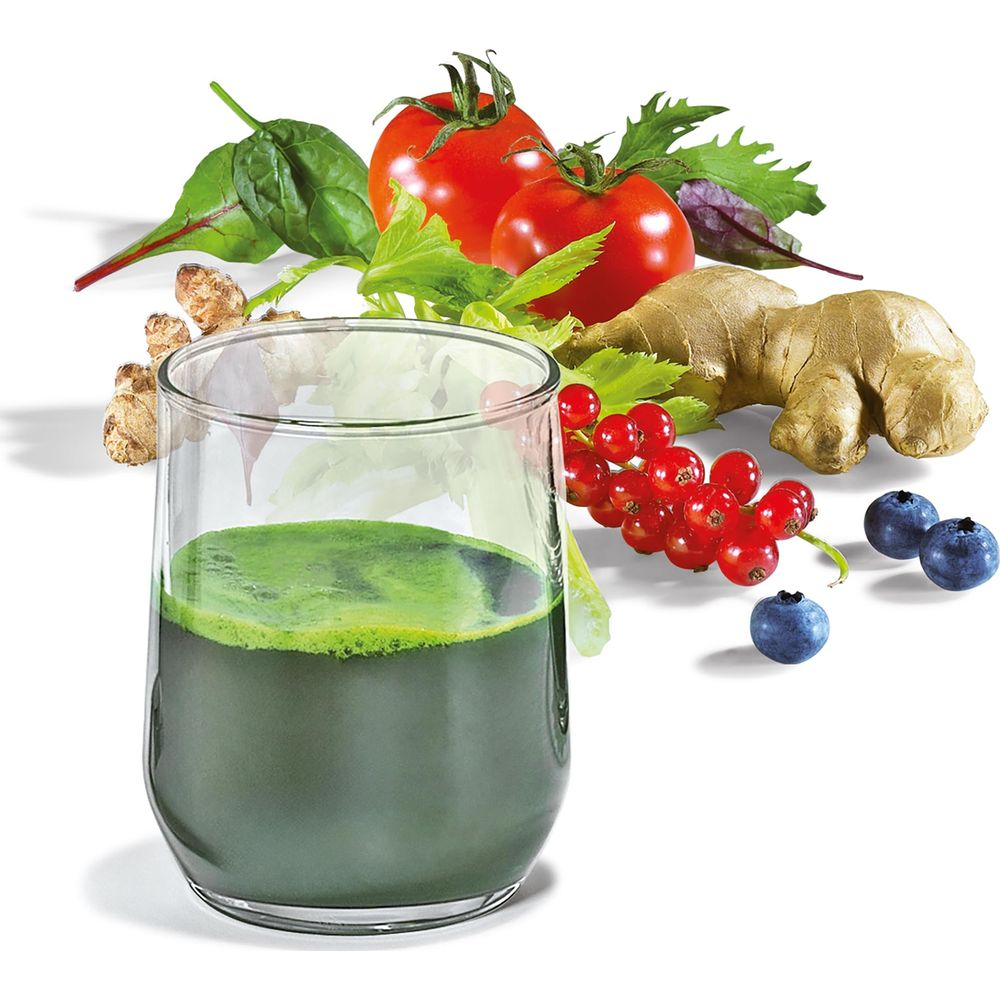 Un verre de jus vert à côté de tomates, de gingembre, de groseilles et de myrtilles.